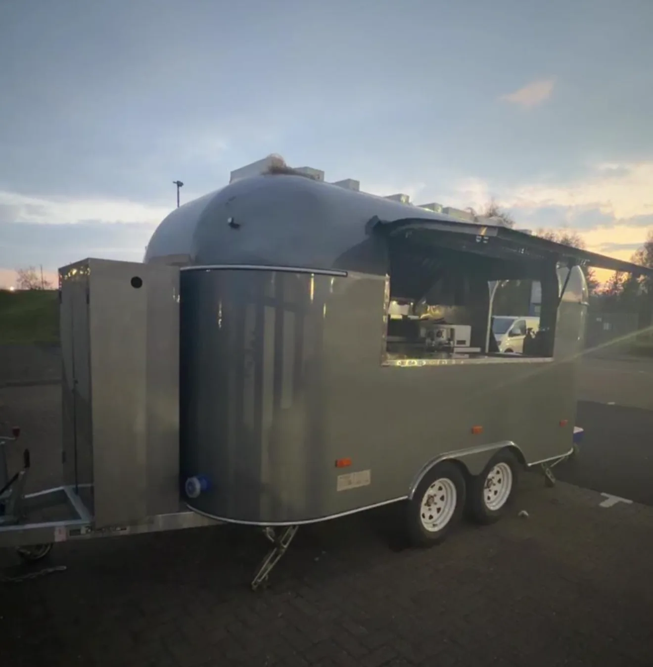 The metallic grey Airstream at dusk, its hatch open