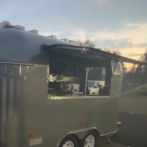 The metallic grey Airstream at dusk, its hatch open and the kitchen lit